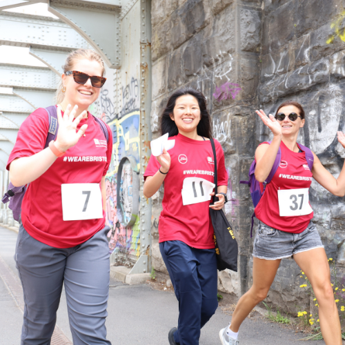 Three people smiling and waving at the camera on a walk. All people are wearing a red #WeAreBristol t-shirt