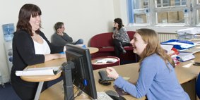 2 people chatting over a reception desk, while in the background, two people chat on sofas