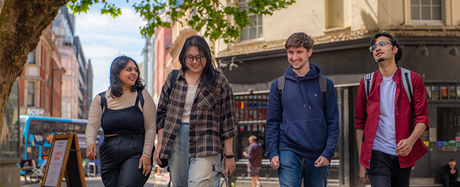 Four young people, two femme-presenting to the left, two masc-presenting to the right, walk along a Bristol street together looking effortlessly cool.