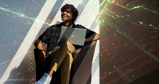 Person sitting in a modern armchair using a Dell laptop, with colorful light reflections creating a prismatic effect on the wall and surroundings.