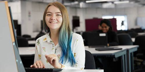 PG student smiling at their desk.