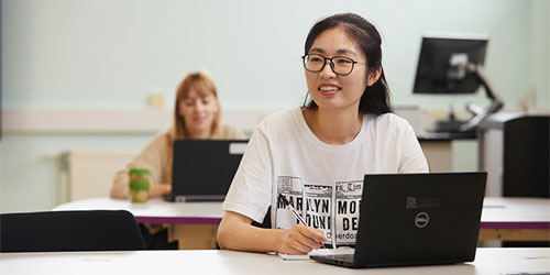 2 students working on their laptops in a teaching room. 