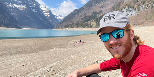 Espen Knoop sits on a rocky bank smiling with mountains in the background