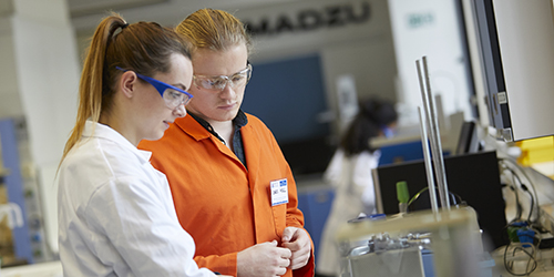 Two students wearing safety goggles working together in a laboratory class.