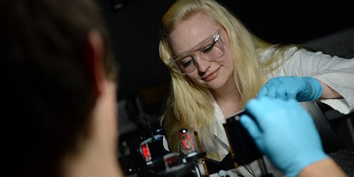 A student wearing safety goggles and blue gloves using some equipment.