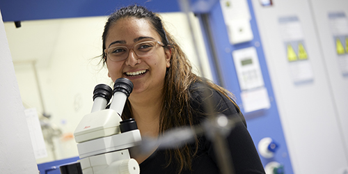 A smiling student looking up from a microscope they are using.