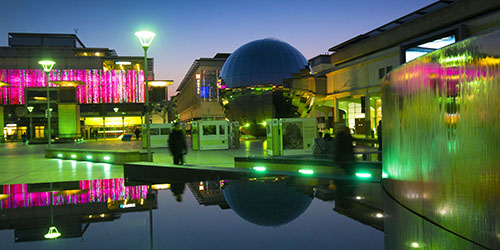 Millennium Square in Bristol lit up in pink and green neon lights at night.