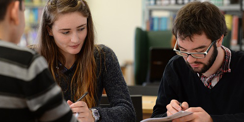 Two students sit together taking notes.