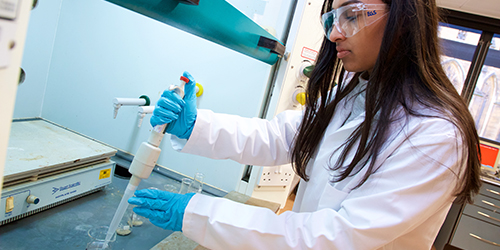 A person in a lab coat and protective eyewear works in a laboratory.