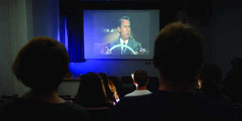 The backs of people's heads as they watch a classic film in a small cinema.