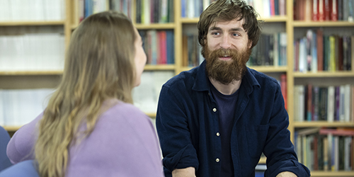 Two people sat having a conversation in a library. 