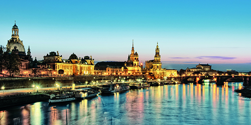 Buildings and boats on a river in a European city are lit up at night. 