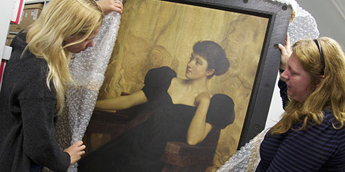Two people remove bubble wrap from a large oil painting