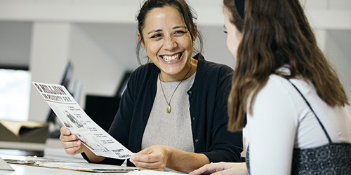 Two students smiling at one another while holding an historical poster.