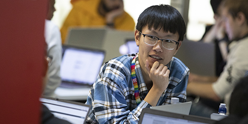 A student sat in a room filled with other students working on their laptops.