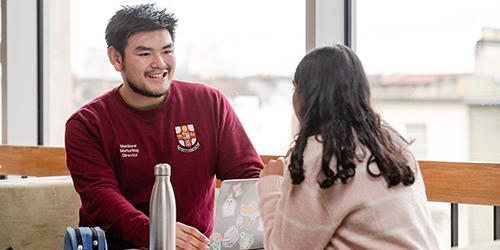 Two students engaged in conversation over a laptop