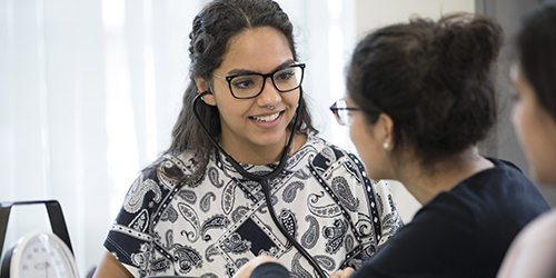 A person wearing a stethoscope around their neck talking to someone.