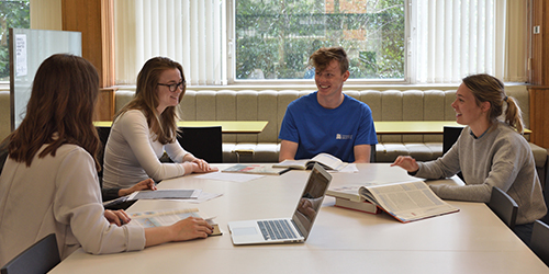 Four people with laptops and books sitting around a table.