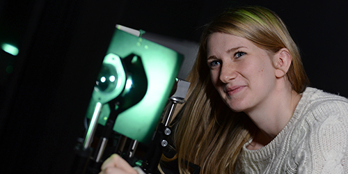 A person looking through a lens in a dark room lit up with a small green light.