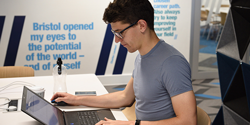 A person working at their laptop in a study area. There is a quote on the wall behind, reading