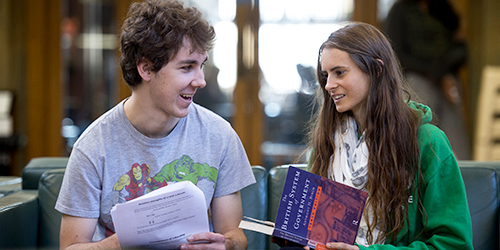 Two people holding a book and some papers chatting.