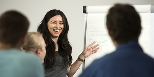 A person pointing at a flipchart and speaking to a group.