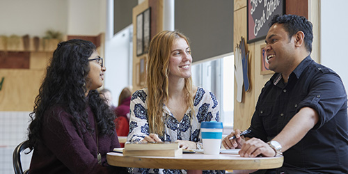 Students sitting around a table with books and a reusable coffee cup.