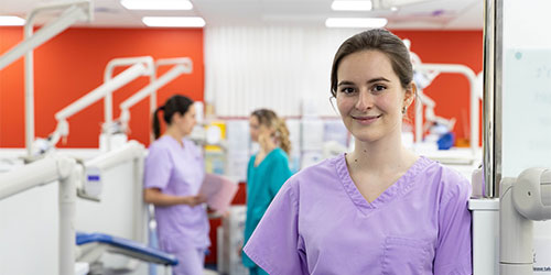 A dental student in a practical laboratory smiling at the camera.