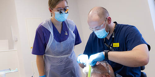 A dental student watching a tutor work on a patient