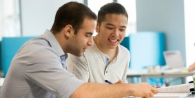2 people sitting together looking at a piece of work, one showing something to the other.