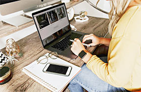 A woman accesses an online lecture on her laptop. Beside her is a notepad.