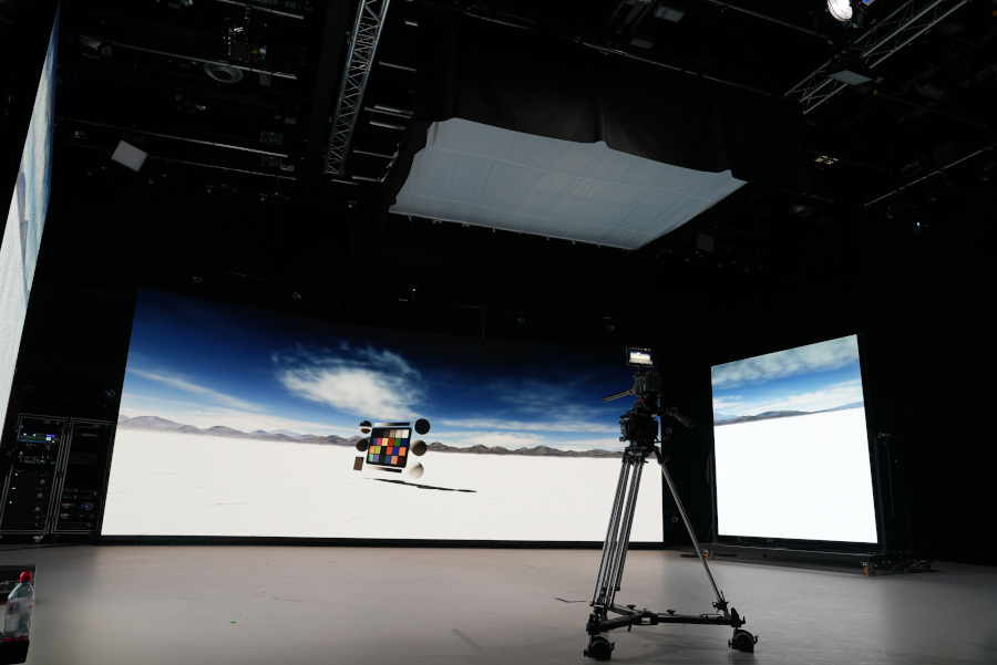 large open studio space with a floor to celling screen with an image of mountains and clouds. In the foreground there is a camera on a tripod.