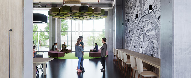 A room with 3 people standing in a group in the foreground an others sitting at a seating area near a window in the background.