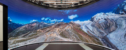Massive curved screen showing mountain landscape against blue sky
