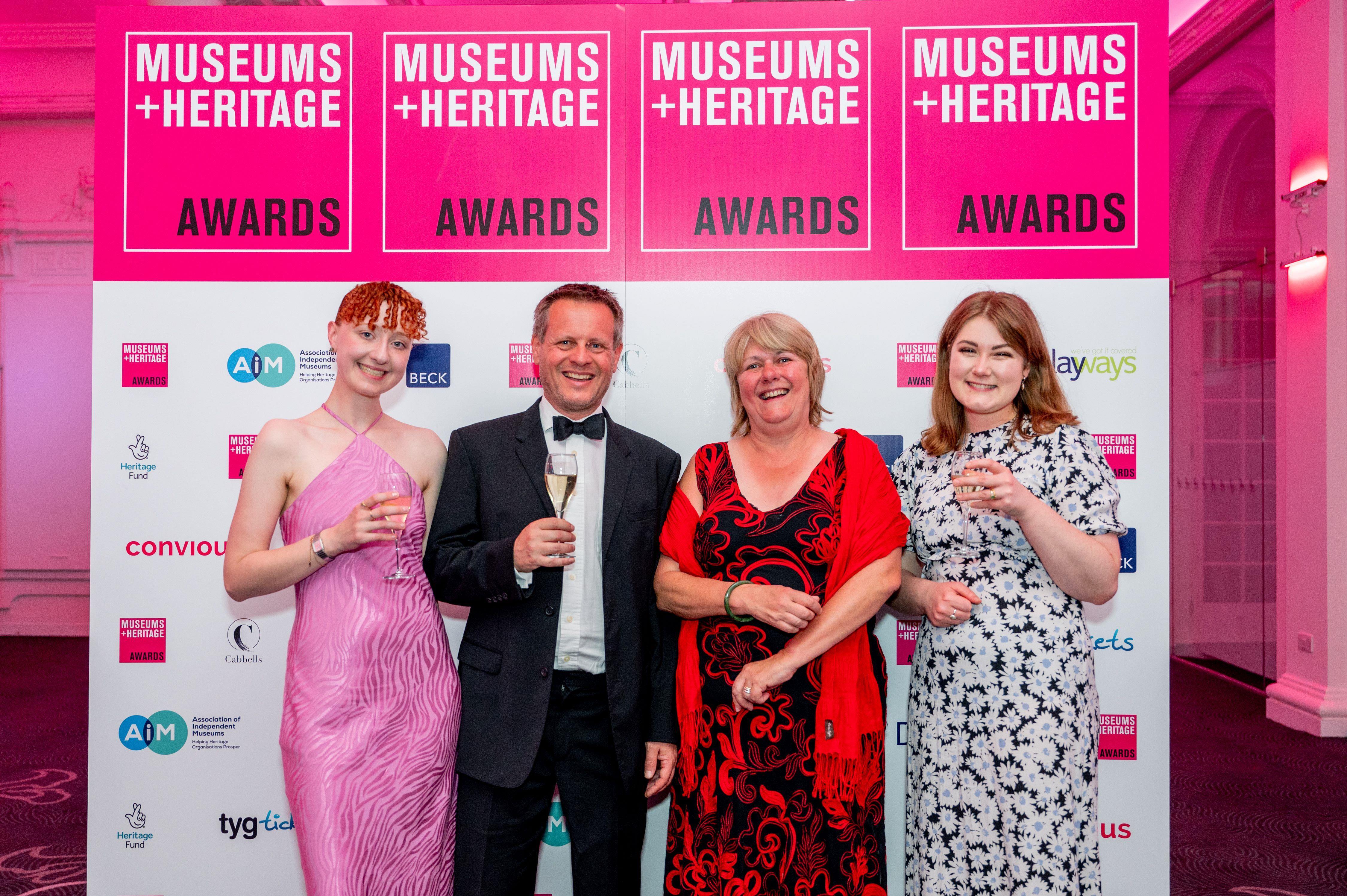 Four people standing in front of a museum and heritage awards backdrop