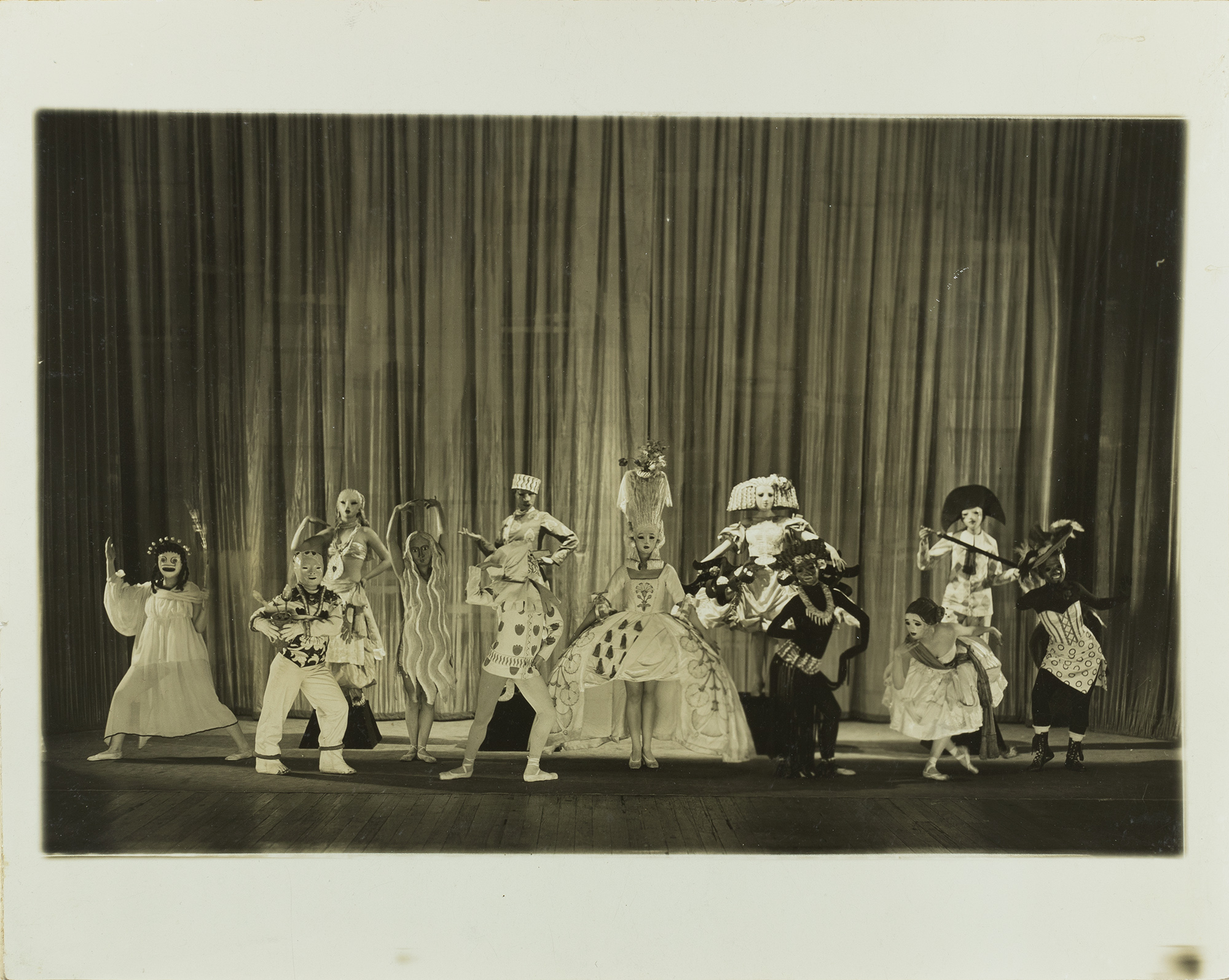 a sepia photograph of a stage with many actors all wearing elaborate masks