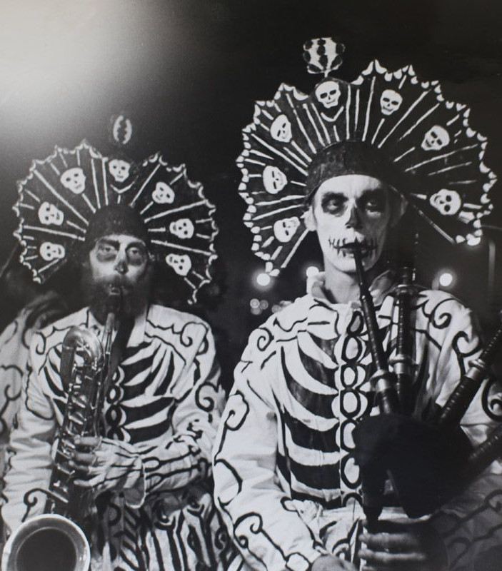 Two men in skeleton style costumes playing saxophone and bagpipes respectively