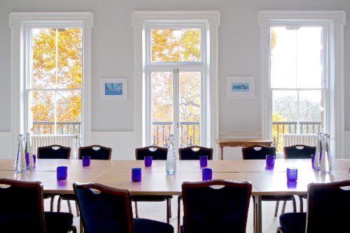 Image of tables and chairs in a meeting rooms with windows in the background