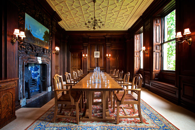 Large room with high ceilings, dark wood panels, large wood table with chairs and chandelier 