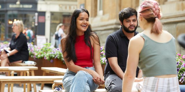 Three students happily chatting while sitting down outside